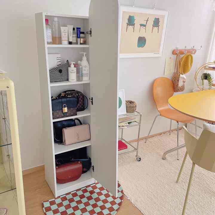 Bright white and yellow toned dining room featuring a modern interior with an open storage cabinet displaying bags and skincare products