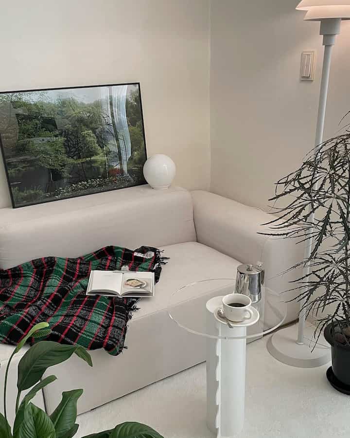 ホワイトトーンのリビング、ホワイトのソファと透明なテーブル、フロアランプ、植物が配置された自然で落ち着いた雰囲気のインテリア