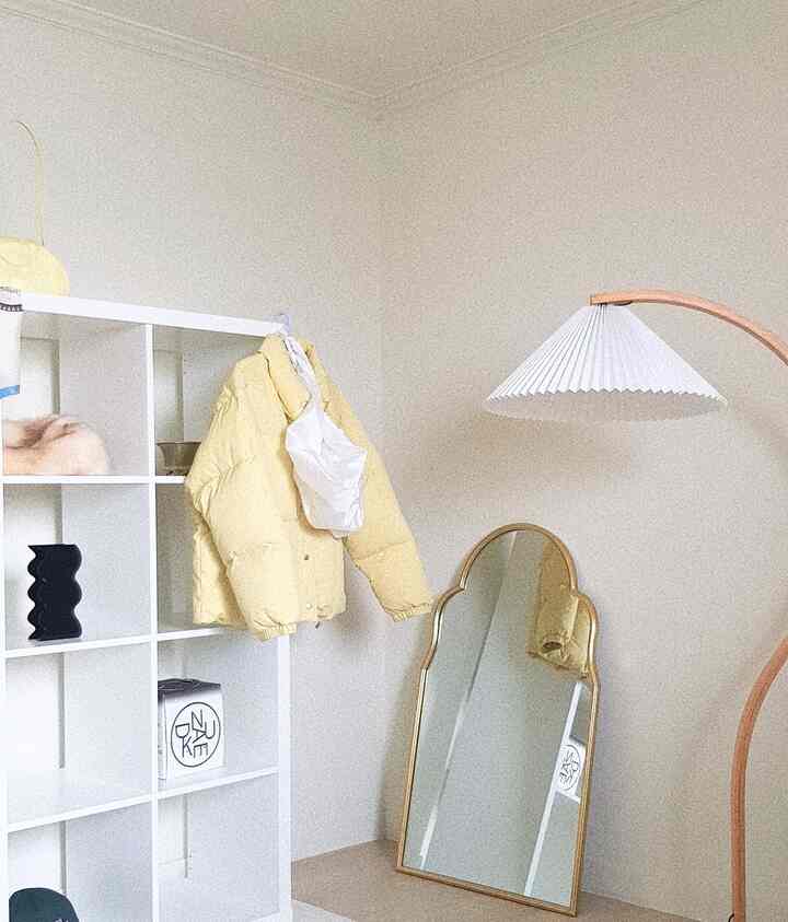 White-toned walk-in closet featuring a white IKEA storage unit and gold-framed mirror in a simple, minimal space