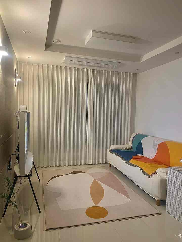 明るいホワイトトーンのコンパクトなリビング、シンプルなソファと抽象柄のラグが配置されたモダンなインテリア