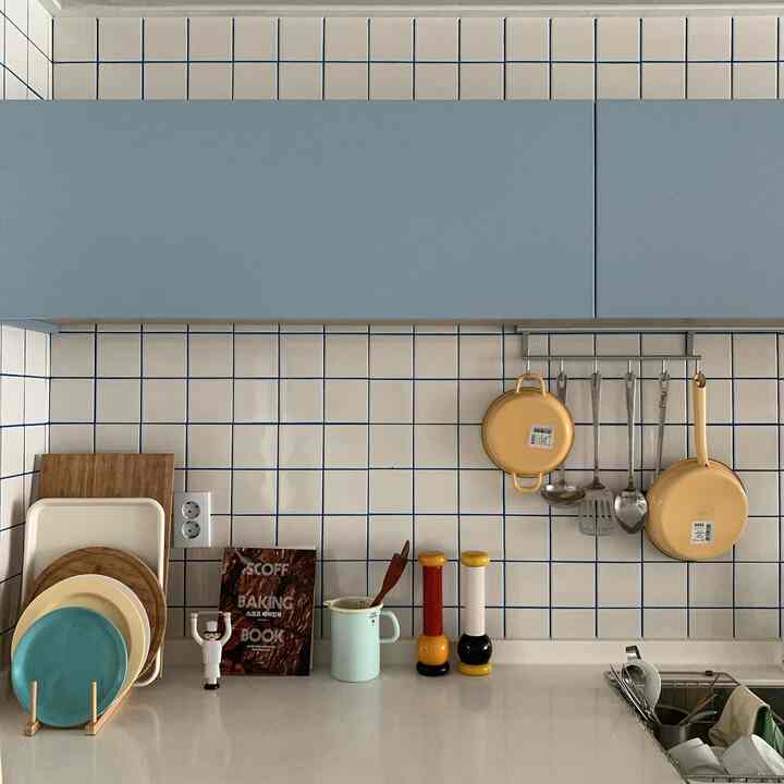 白と青のキッチンスペース、黄の調理器具と多彩な皿が整然と配置されたミニマルなインテリア