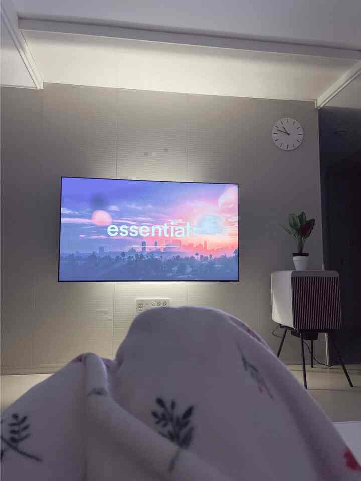 White and beige toned living room with wall-mounted TV and cozy blanket, creating a warm and comfortable atmosphere