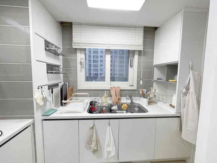 ホワイトとグレーのトーンのキッチン、シンク周りに整理された調理器具とエプロン、タオルが配置された生活感のある清潔な空間