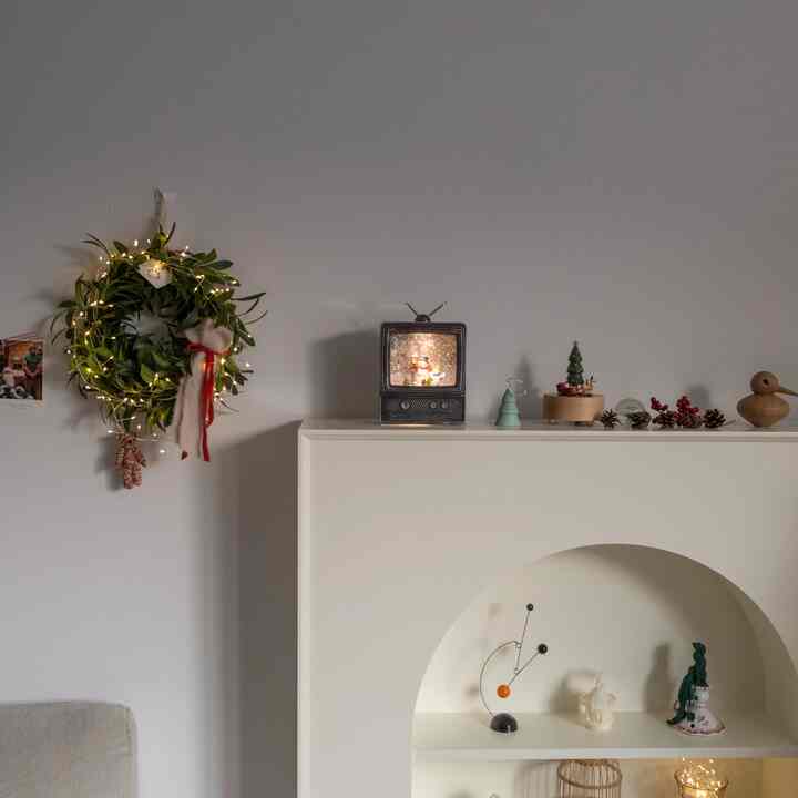 Natural-toned living room with white wall and mantel console shelf, decorated with a Christmas wreath and various objets creating a warm festive atmosphere