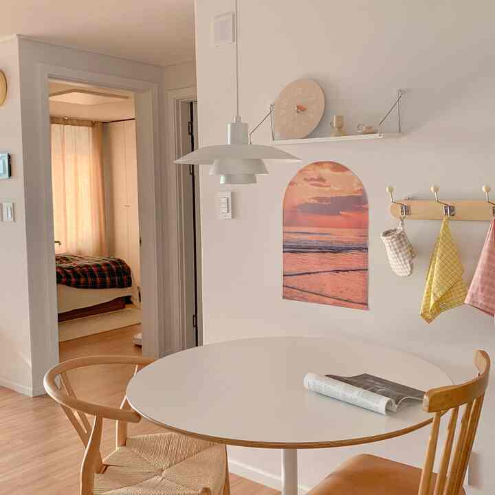 Natural-toned kitchen space with warm wood chairs, white round table, and wall featuring arch poster and shelf