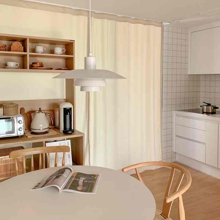 クリーム色のカーテンと木製椅子が配置されたナチュラルなワンルームのキッチン兼おうちカフェスペース