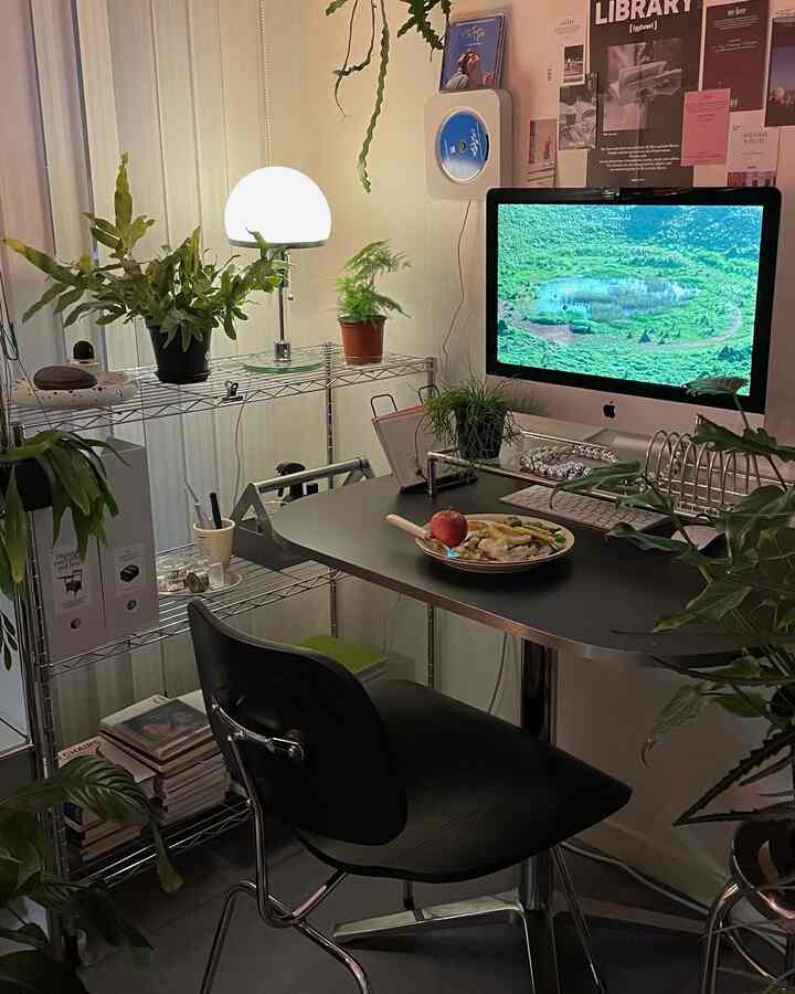 緑の植物が多いコンパクトな空間に黒いデスクとチェアが配置されたモダンなホームオフィス