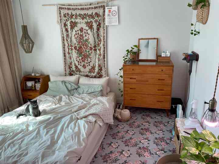 White and wood tone bedroom featuring a cat on the bed, with retro floral rug and tapestry creating a cozy atmosphere