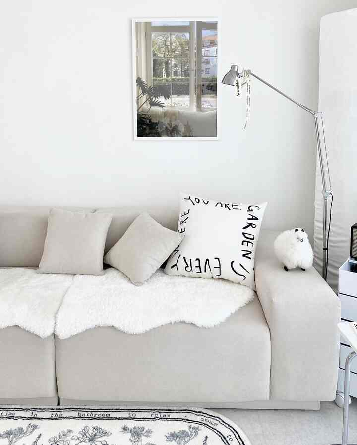 Bright white and gray toned living room featuring a sofa, cushions, and poster creating a modern, natural atmosphere