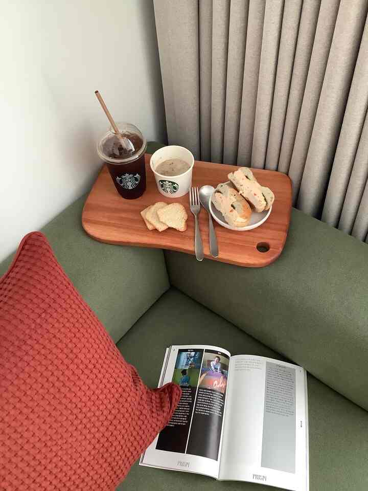 Natural color toned bedroom space featuring green fabric sofa, wood tray with food and red cushion, creating a cozy home cafe vibe