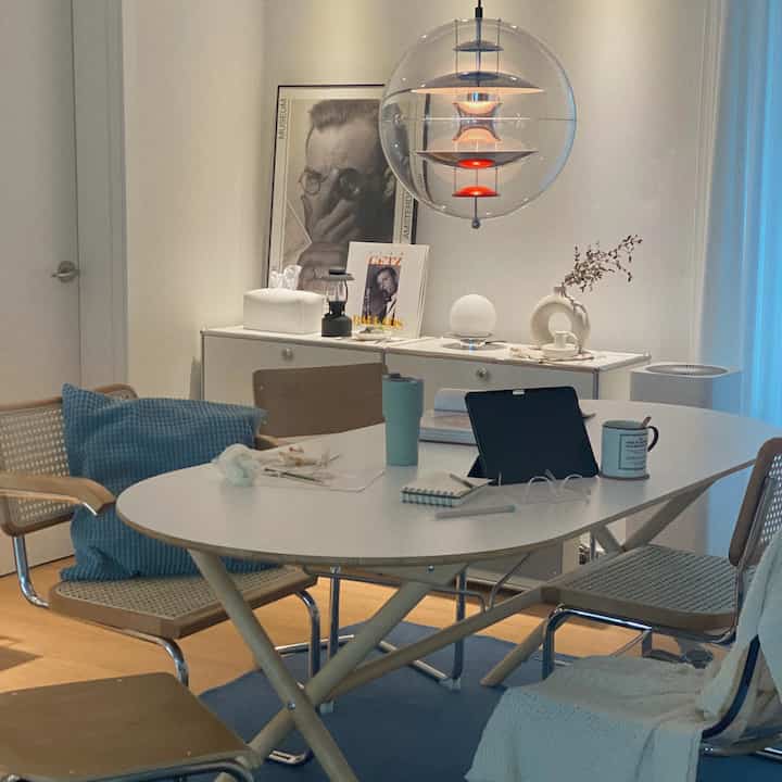 A white and natural wood toned dining room featuring a modern mid-century dining table and rattan chairs in a cozy setting