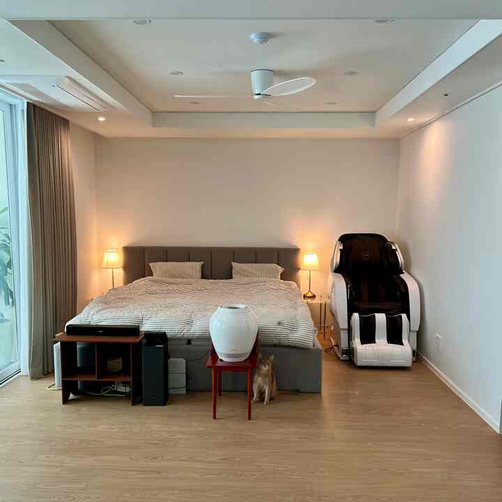Simple and modern bedroom featuring a gray bed and wood tone flooring, with antique nightstands, a humidifier, and massage chair arranged neatly