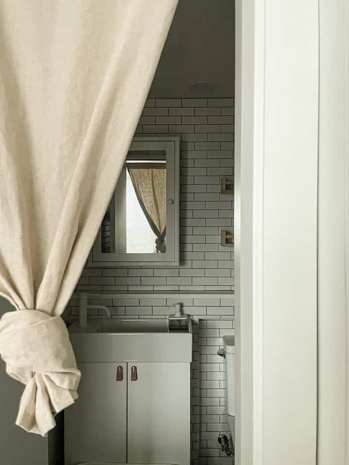 白とベージュの色調のバスルーム、洗面台と仕切りカーテンが配置されたシンプルでモダンなインテリア