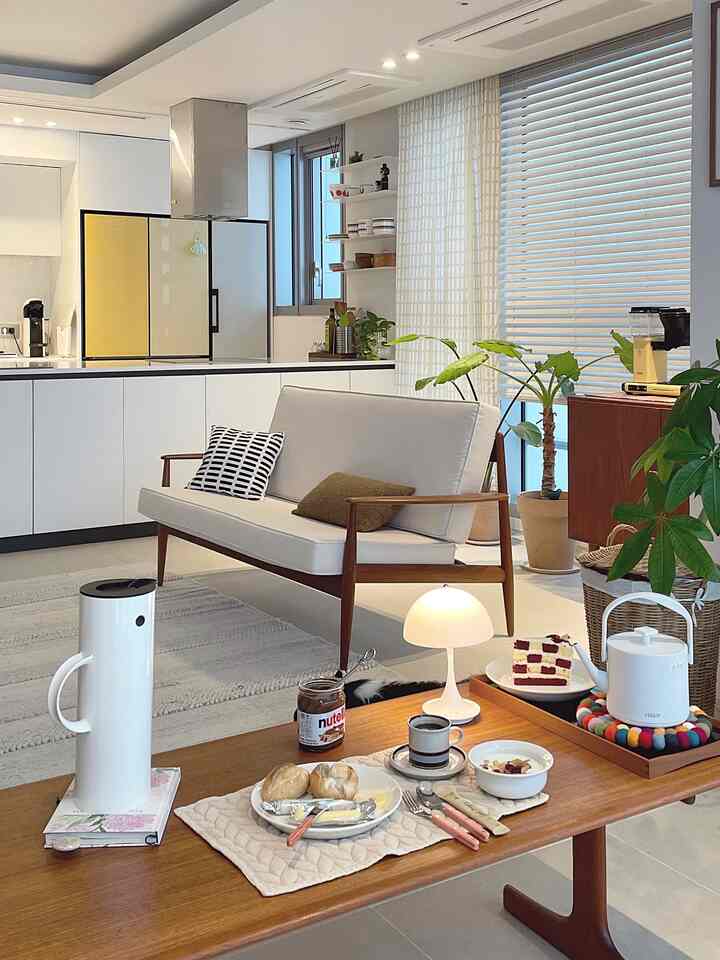 A white and natural toned living room combined with kitchen featuring wooden sofa and coffee table creating a cozy atmosphere