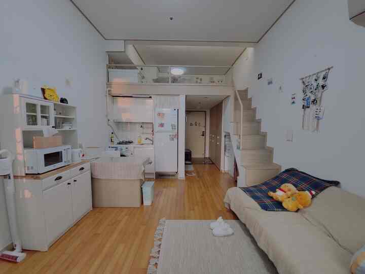 Natural-toned loft studio featuring wooden floor, sofa, stairs, and kitchen blended in a cozy and spacious atmosphere