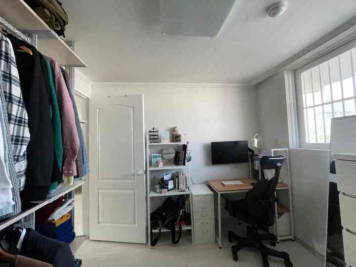 White and natural toned walk-in closet featuring a compact home office with desk, shelving, and organized storage