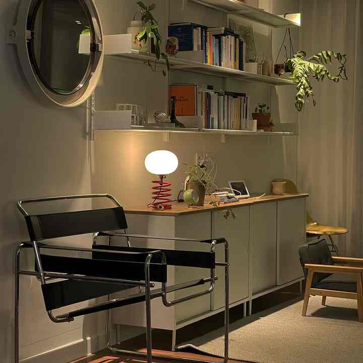 Living room with white walls and shelves, featuring a black mid-century modern armchair and a red table lamp in a warm ambiance