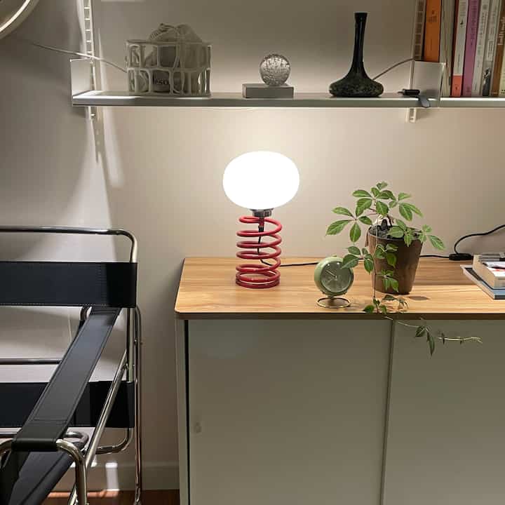 A modern study space in wood tones and white featuring shelves with objects, table lamp, and a potted plant, creating an organized atmosphere