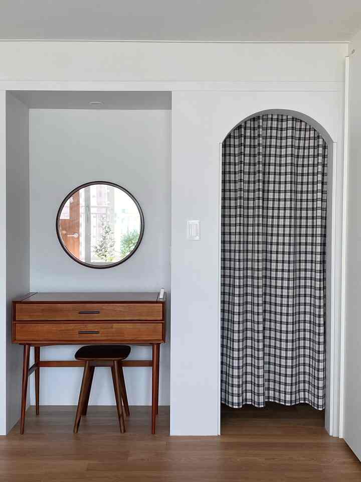 白い壁と木目調の化粧台、黒のチェック柄カーテンが配置されたアーチ型の扉のある印象的な寝室