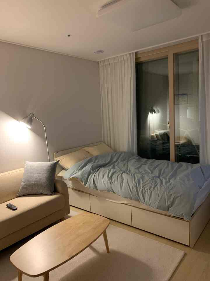 Minimal single household veranda room in white and beige tones, featuring bed, sofa, and table arranged neatly in a cozy interior