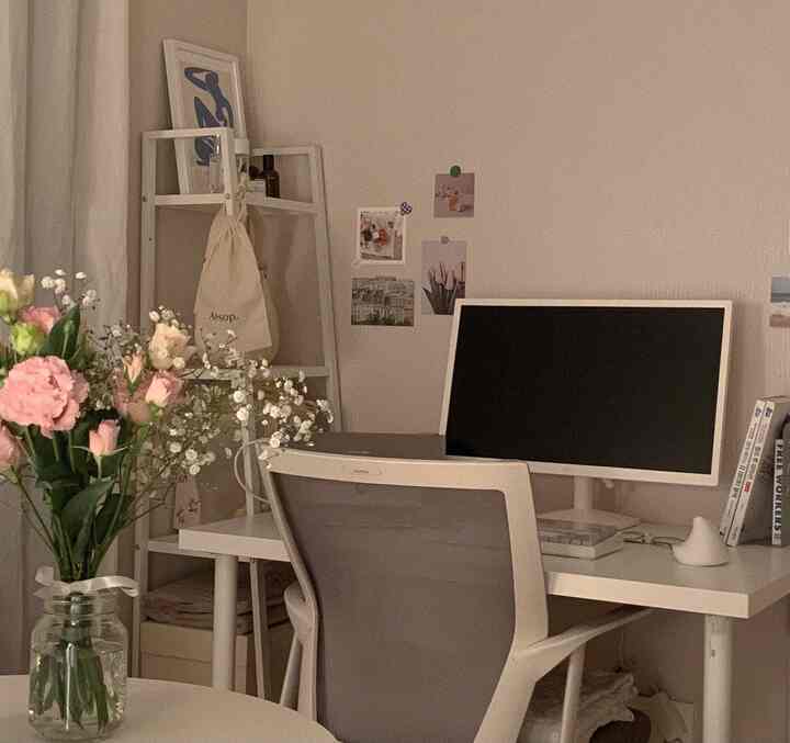 Beige and white toned small home office with simple desk and chair, flowers adding a cozy atmosphere