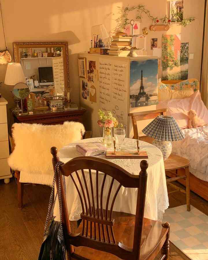 暖かいナチュラルカラーのヴィンテージスタイルの寝室兼ダイニング、円形テーブルと木製ダイニングチェアが配置された雰囲気のある空間