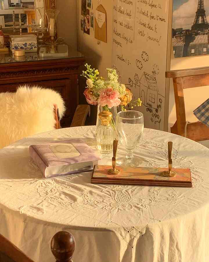 温かい陽射しが差し込む、白いテーブルクロスが掛けられた丸テーブルのダイニングルーム、花瓶と椅子が配置された心地よい空間