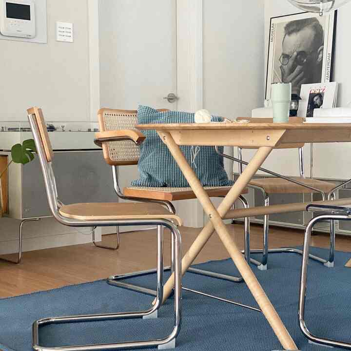 Wood tone and blue dining room featuring a wood dining table, rattan chairs, large framed artwork, and a blue rug in a modern home cafe setting