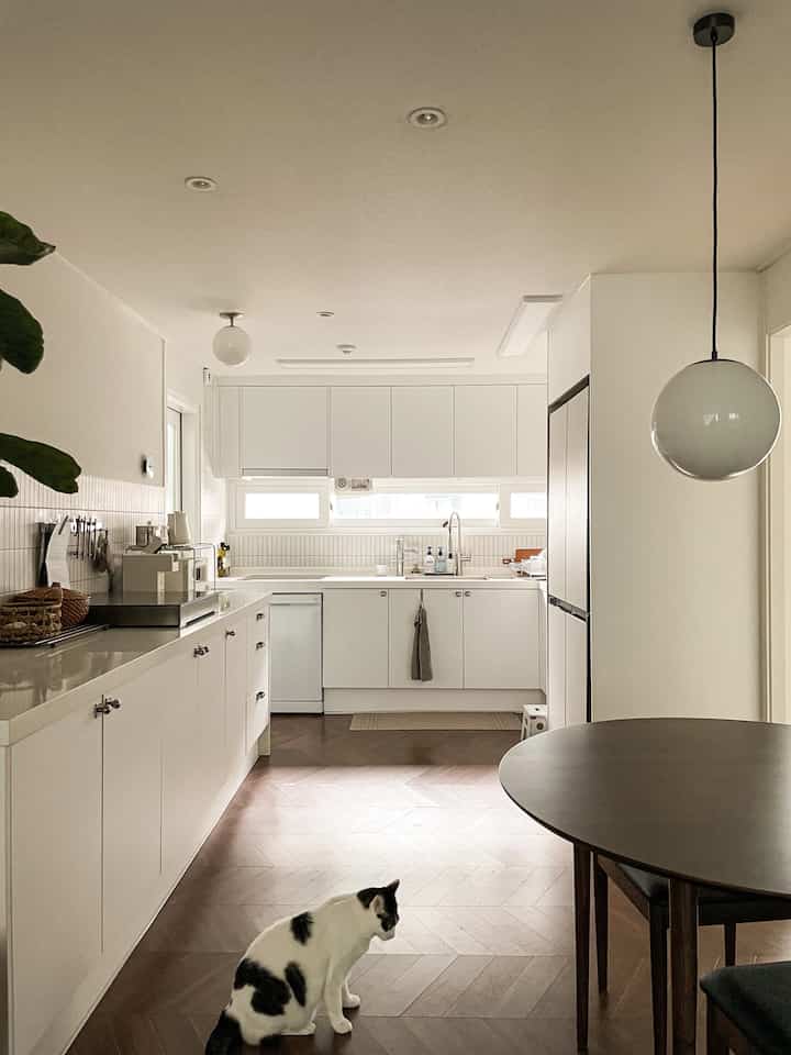 White and natural toned kitchen space featuring wooden dining table and chairs, with a cat on herringbone floor creating a cozy, clean atmosphere