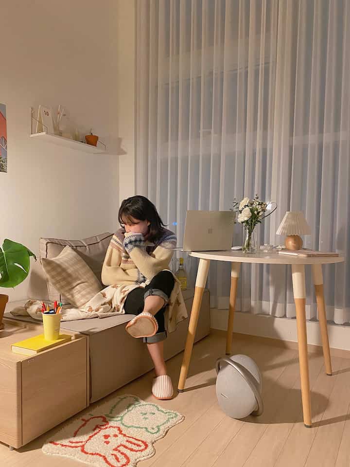 White and natural-tone studio living room featuring beige sofa and round table with laptop, creating a cozy and comfortable atmosphere