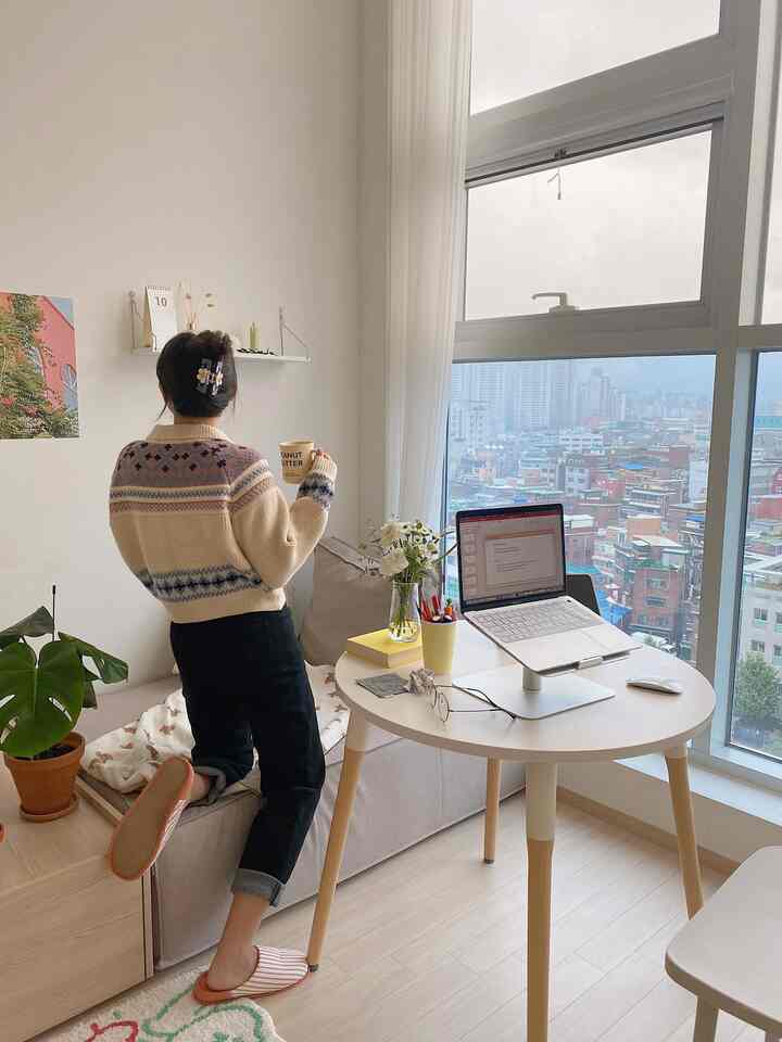 Bright white and natural-toned studio home office with a round table, sofa bed, large window, and curtains creating a cozy atmosphere