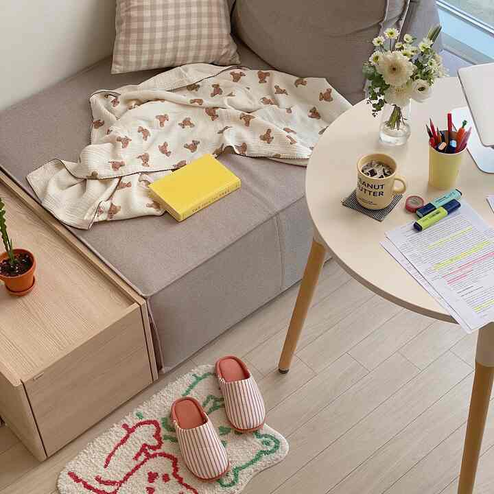 Beige and white toned small studio apartment featuring cozy sofa, round table, and desk creating a comfortable home office space