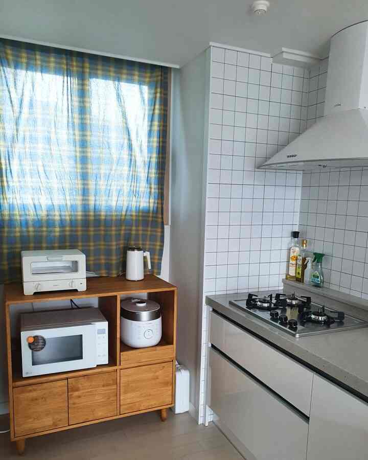 Cozy kitchen featuring white surfaces and wood cabinetry complemented by blue and yellow checkered curtains