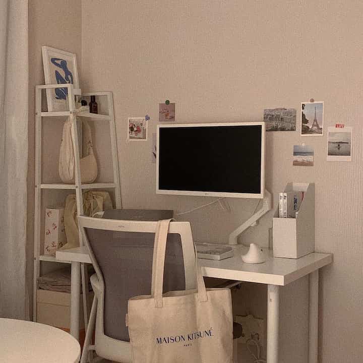 White and beige toned home office featuring a monitor, office chair, and shelving with a simple and clean workspace