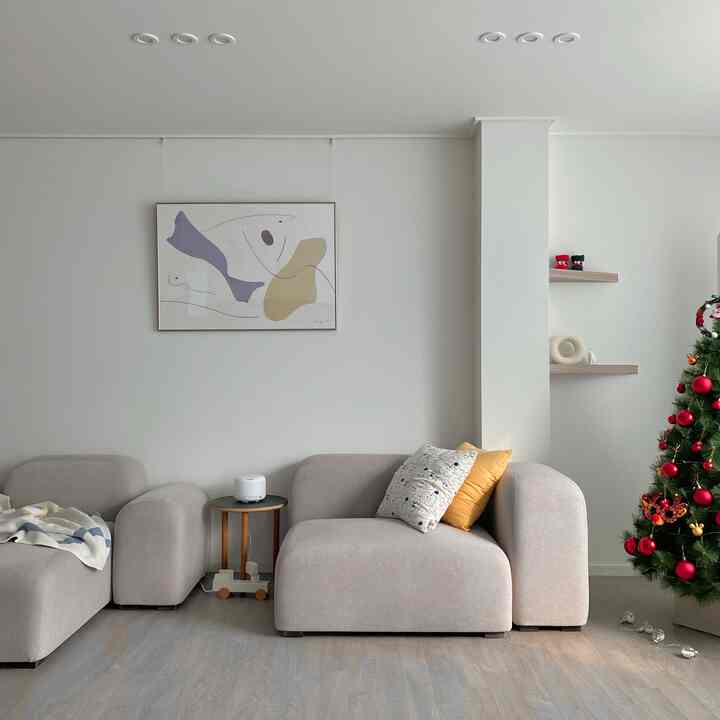 白い壁と木目調の床のリビング、ベージュのコーナーソファとクリスマスツリーが配置された、落ち着いた雰囲気のあるナチュラルモダンな空間