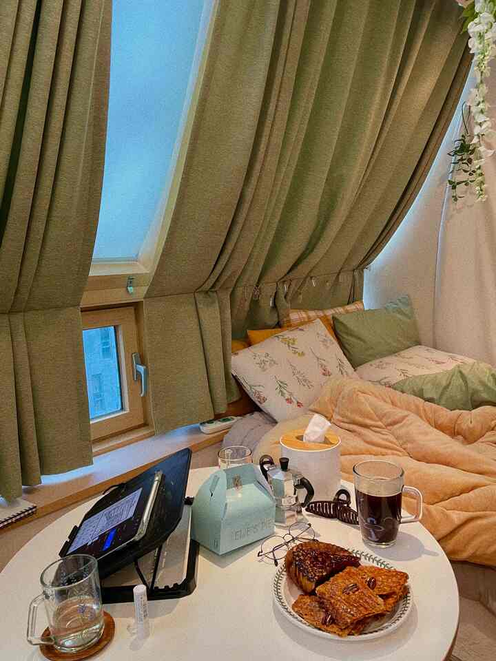 Cozy bedroom with green blackout curtains and round table featuring bedding and coffee creating a warm atmosphere