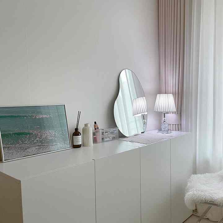 White-toned bedroom vanity space featuring a storage cabinet, an organic-shaped mirror, and a picture frame creating a clean interior