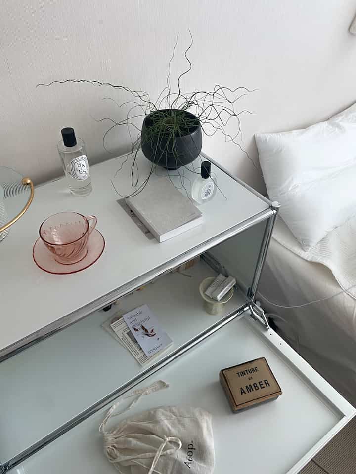Bright white and natural toned bedroom space featuring nightstand with plant and diffusers, embodying a simple minimalistic atmosphere