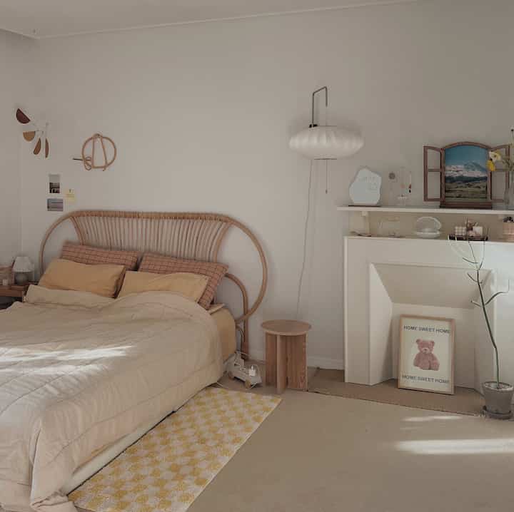 Beige-toned bedroom featuring a rattan bed headboard, fireplace console, and yellow checkered rug with a cozy atmosphere