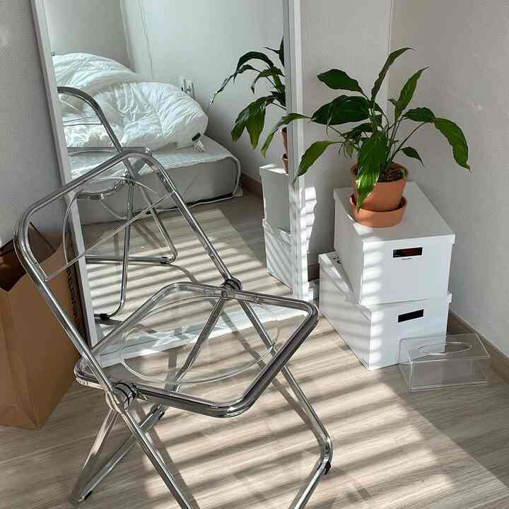 ナチュラルな色調と透明な家具が映えるコンパクトな寝室の一角、収納ボックスの上に植物が置かれている印象的な空間