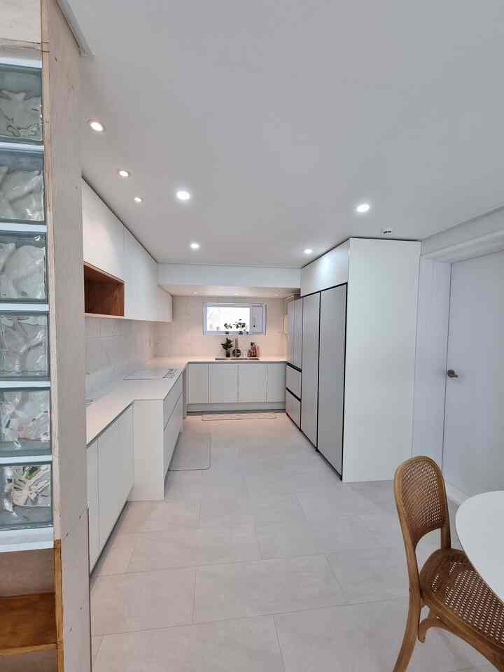 Bright and clean kitchen connected to veranda featuring custom white cabinetry and wood-toned dining chair