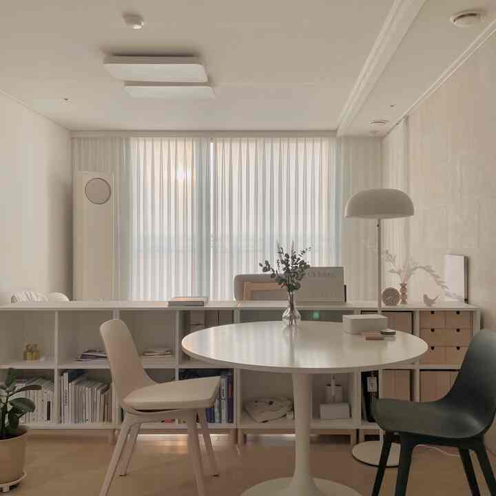 Soft white and natural toned dining room featuring a central round dining table and chairs with sheer curtains, creating a clean and cozy atmosphere