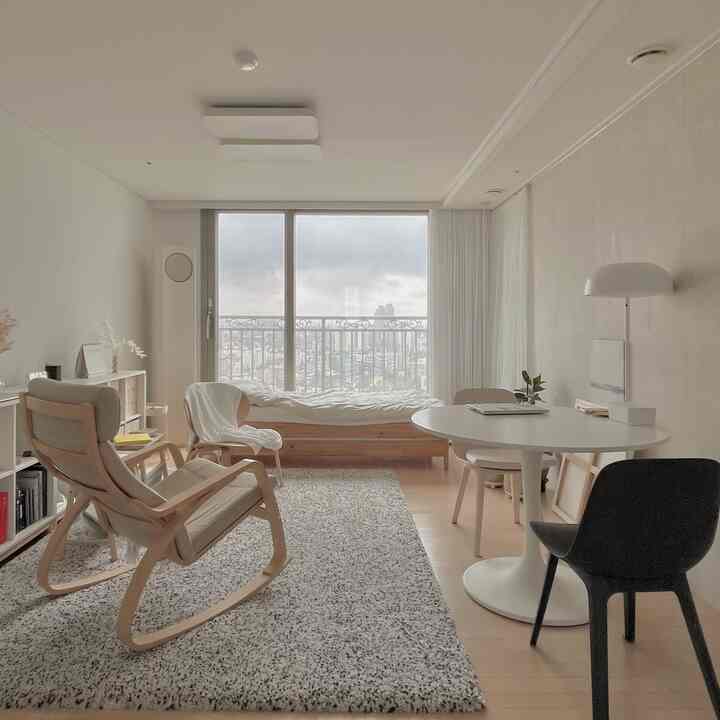 Bright white and wood tone studio apartment living room featuring a daybed, armchairs, and a round dining table with a simple natural style