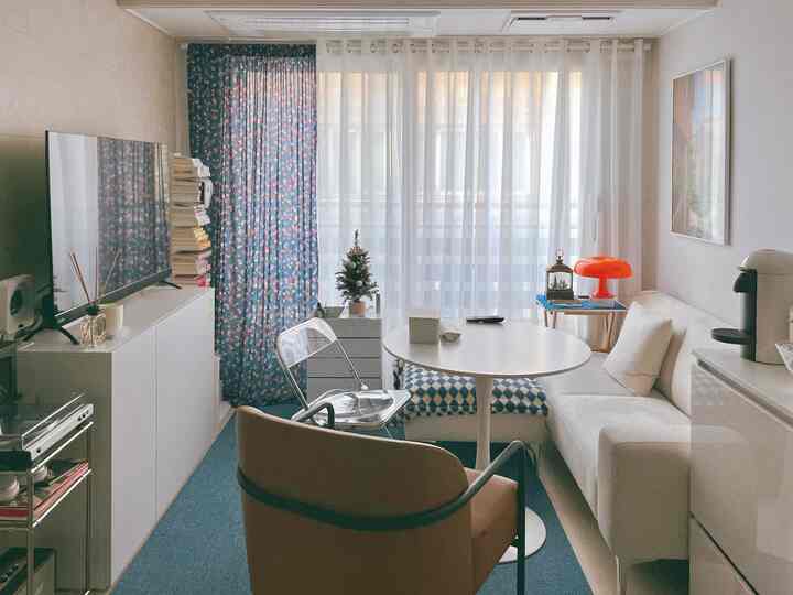 A white and blue toned living room featuring a round table and sofa with an orange lamp accent in a simple modern setup