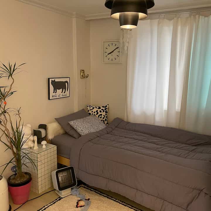 グレーの寝具が印象的なナチュラルトーンの一人用寝室、観葉植物が配置された落ち着いた空間