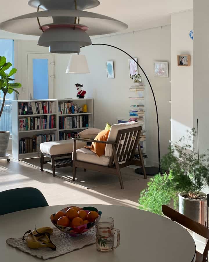 Natural light living room with light brown wooden armchair and white walls featuring a white bookshelf