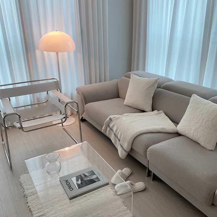 Light gray and white toned living room featuring a sofa, acrylic table, and floor lamp with a cozy modern vibe
