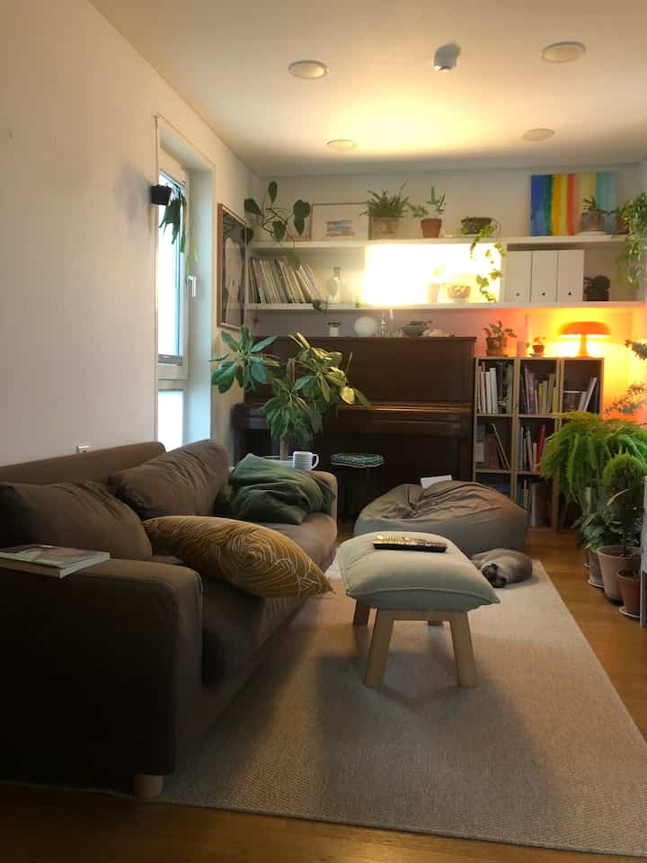 暖かいベージュとブラウンの色調のリビング、快適なソファとビーズクッション、植物とピアノが調和した自然感あふれるインテリア