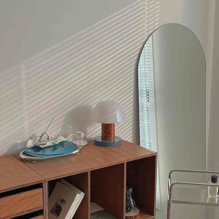 Natural-toned space featuring wooden shelf, full-length mirror, and table lamp with simple interior design