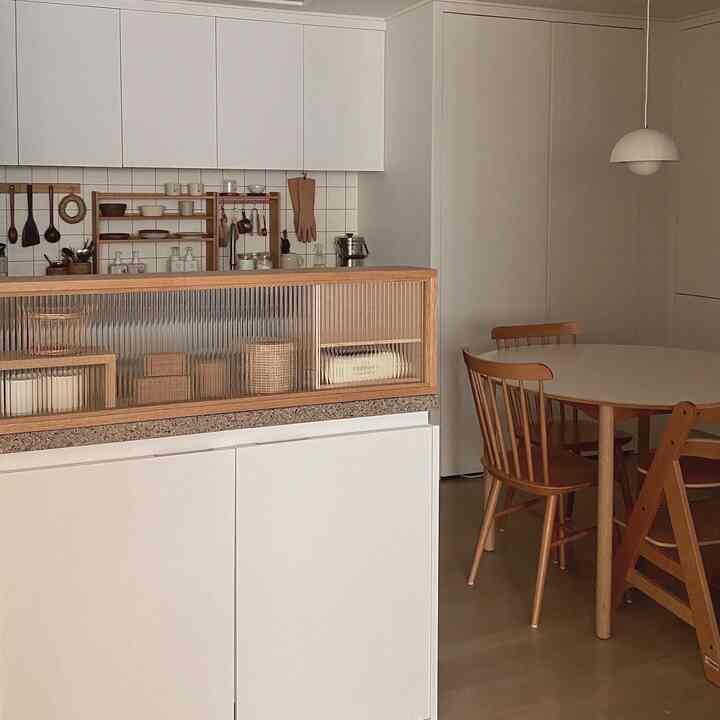 明るい白と温かみのあるオーク材のキッチン、棚と丸いダイニングテーブルが配置された居心地の良い空間